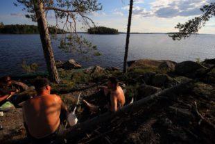 Kesäillan auringonhämy värjää järvenrannalla istuvat ihmiset kullanpunertaviksi.