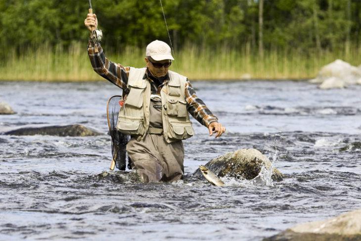 Kalastaja nostaa vapaa ylös, veden pinnalla näkyy nouseva kala. 