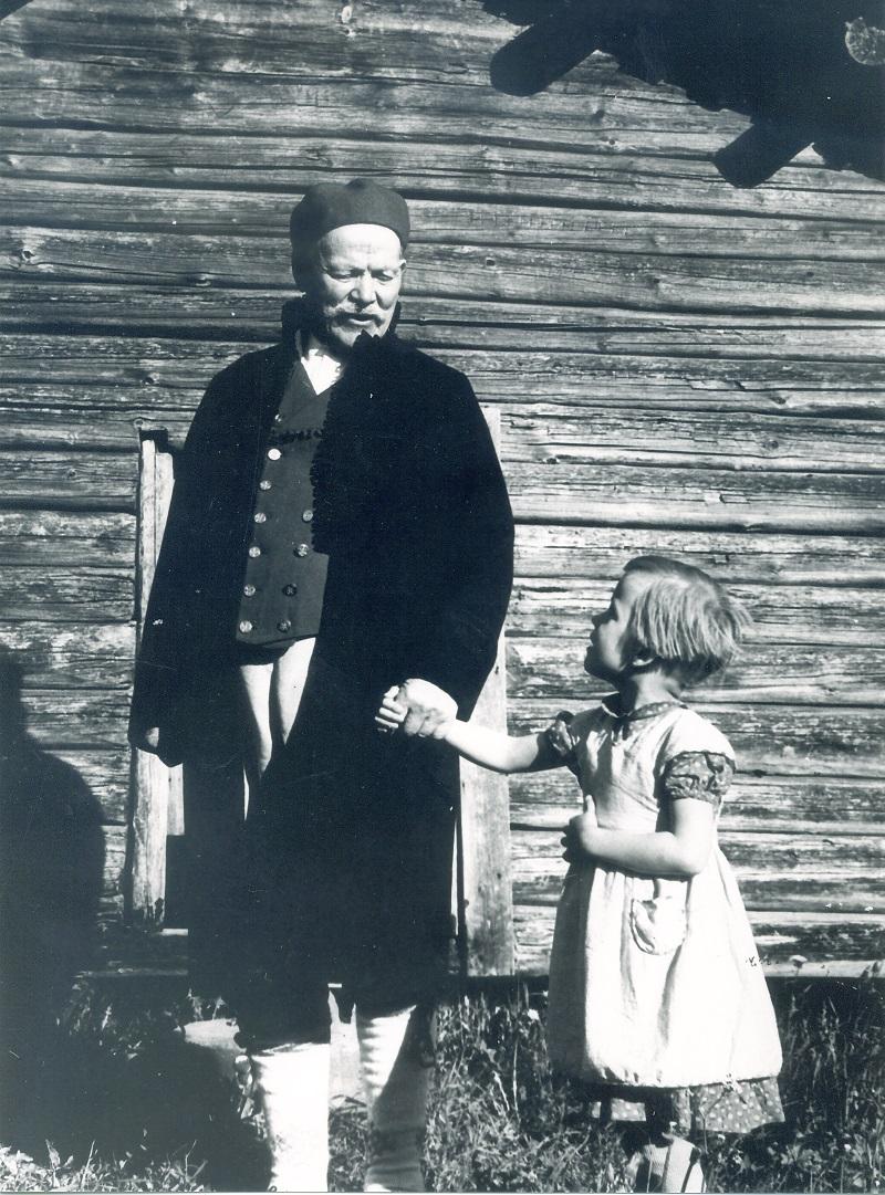 Mustavalkoisessa kuvassa vanhempi mies pitää kädestä valkomekkoista tyttöä Kuva otettu vuonna 1961.
